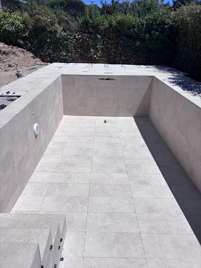 Piscina de hormigón en obra, con azulejos claros y escalera. Expertos en construcción e impermeabilización de piscinas.