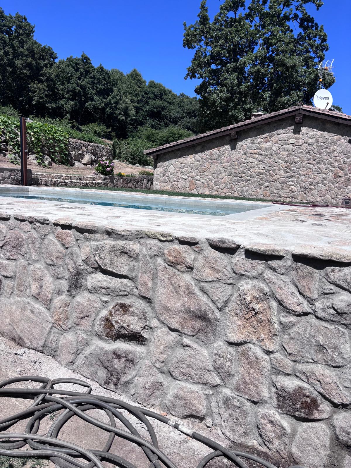 Construcción de piscina de hormigón con impermeabilización. Obra con muro de piedra, rodeada de naturaleza.