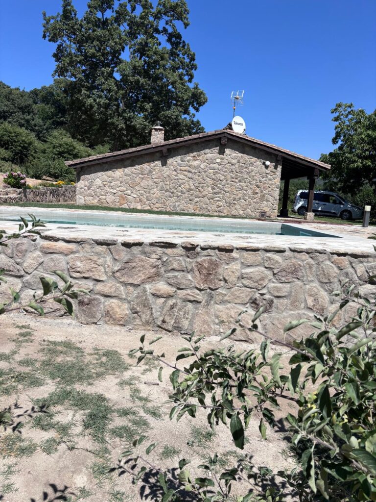 Piscina de obra con muro de piedra y casa. Construcción e impermeabilización de piscinas de hormigón.