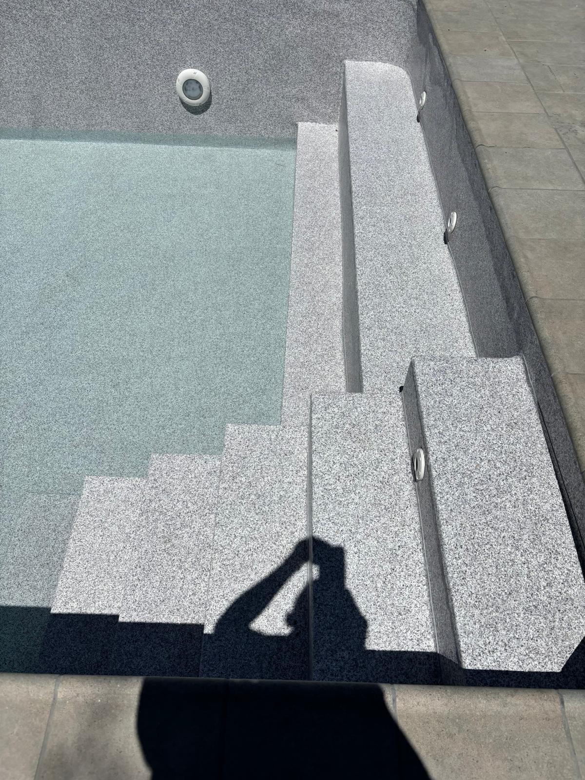Construcción y obra de piscina de hormigón con impermeabilización, escaleras y acabado granulado.